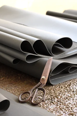 Fogli di PVC grigio accatastati su un banco, accanto a un paio di forbici da sarto