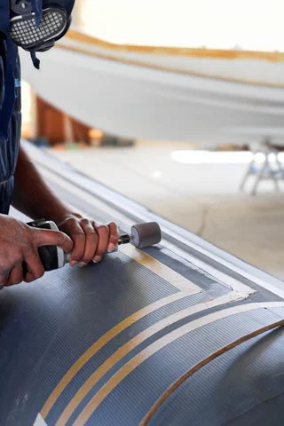 Un rullo abrasivo corre lungo il fianco di un gommone, con lo scafo di una barca sullo sfondo