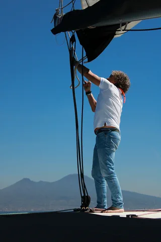 Un marinaio issa la vela, il Vesuvio all'orizzonte
