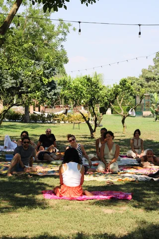 Un gruppo seduto in cerchio sui teli, all'ombra degli alberi di un giardino