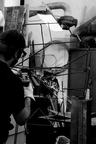 Un fabbro al lavoro con la smerigliatrice: una pioggia di scintille illumina l'officina buia